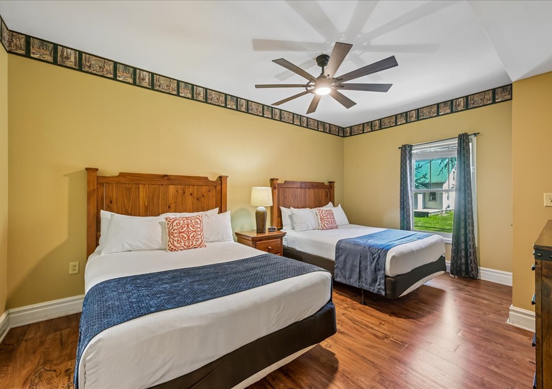 Relax in your comfortable twin bedroom with rich hardwood floors, stylish ceiling fan, and peaceful garden views through your private window.
