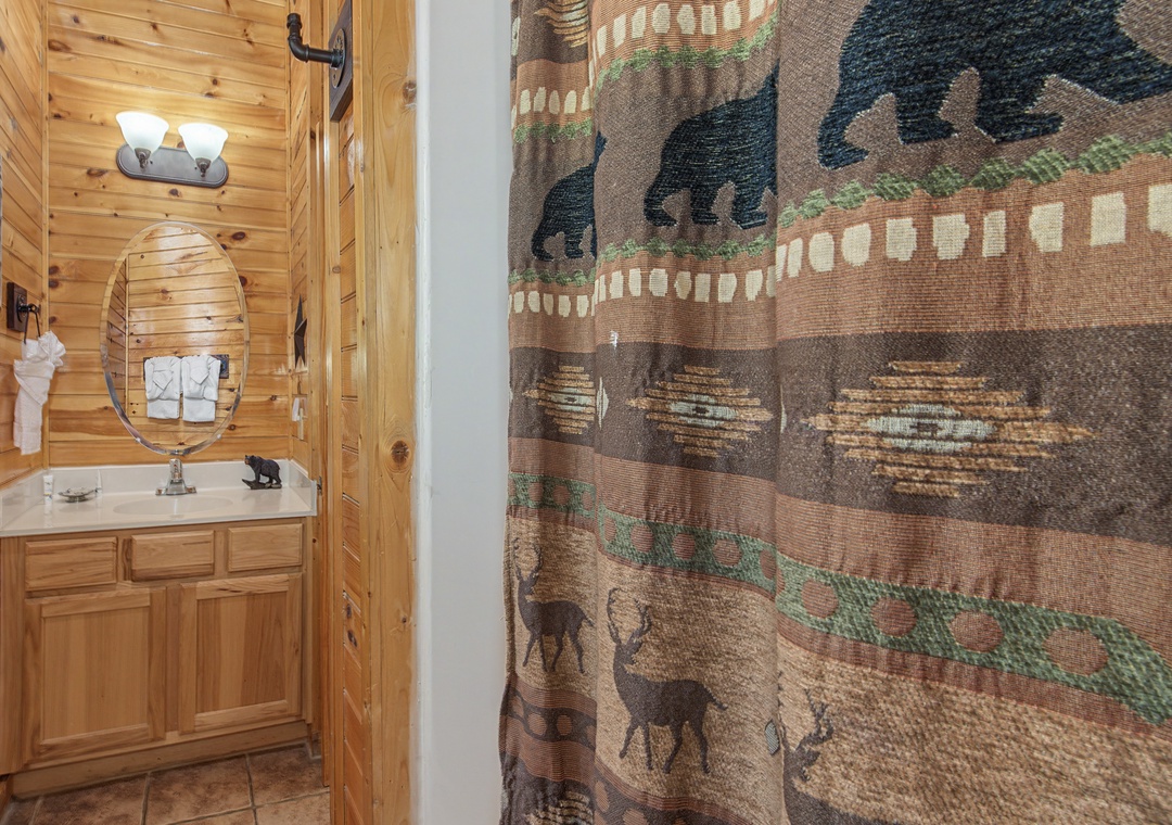 Your rustic bathroom features warm knotty pine walls, charming wildlife-themed shower curtain, and thoughtful amenities for a cozy mountain retreat experience.