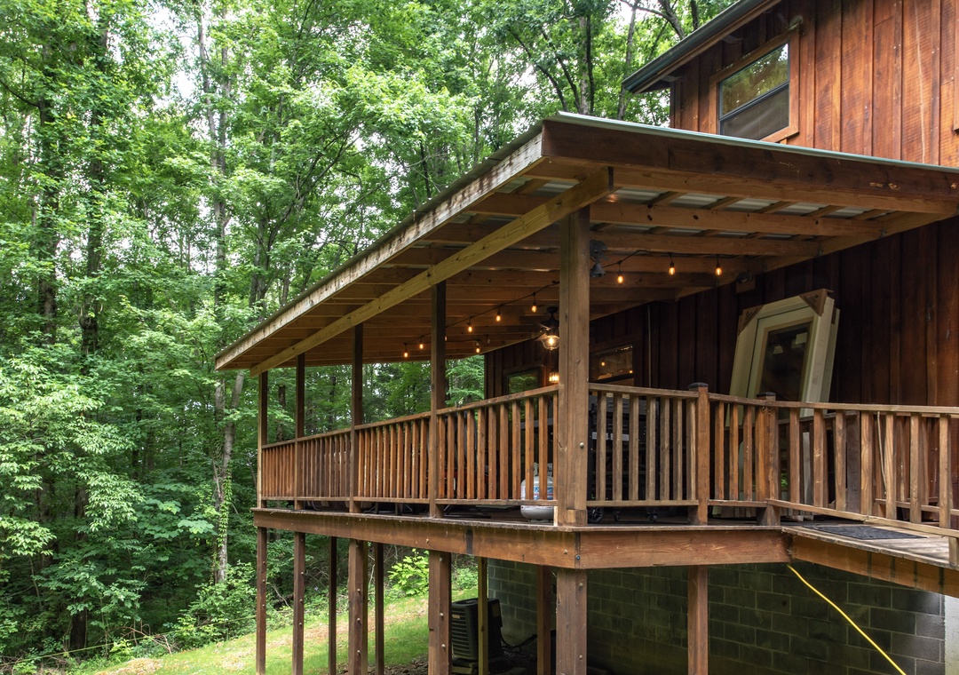 Rustic cedar cabin nestled in a lush forest, featuring a covered deck with string lights for peaceful woodland evenings.