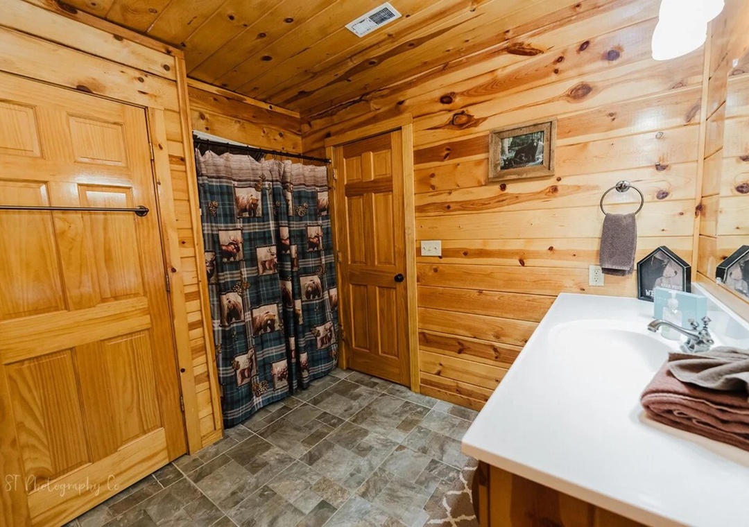 Step into your private bathroom, where knotty pine walls and rustic charm meet modern comfort. Fresh towels await after a refreshing shower in this cozy, cabin-style retreat.