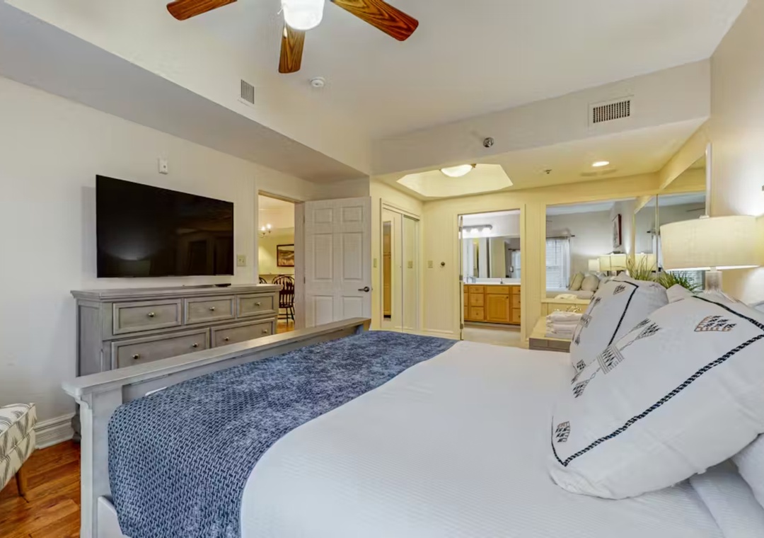 Your master suite welcomes you with a plush bed, warm wooden ceiling fan, and elegant TV setup for cozy evenings.