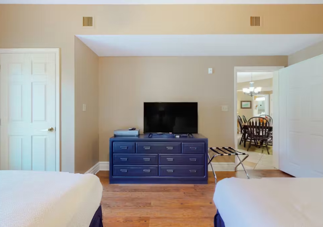 Your spacious bedroom features twin beds, flat-screen TV, and ample storage in a stylish blue dresser for a comfortable stay.