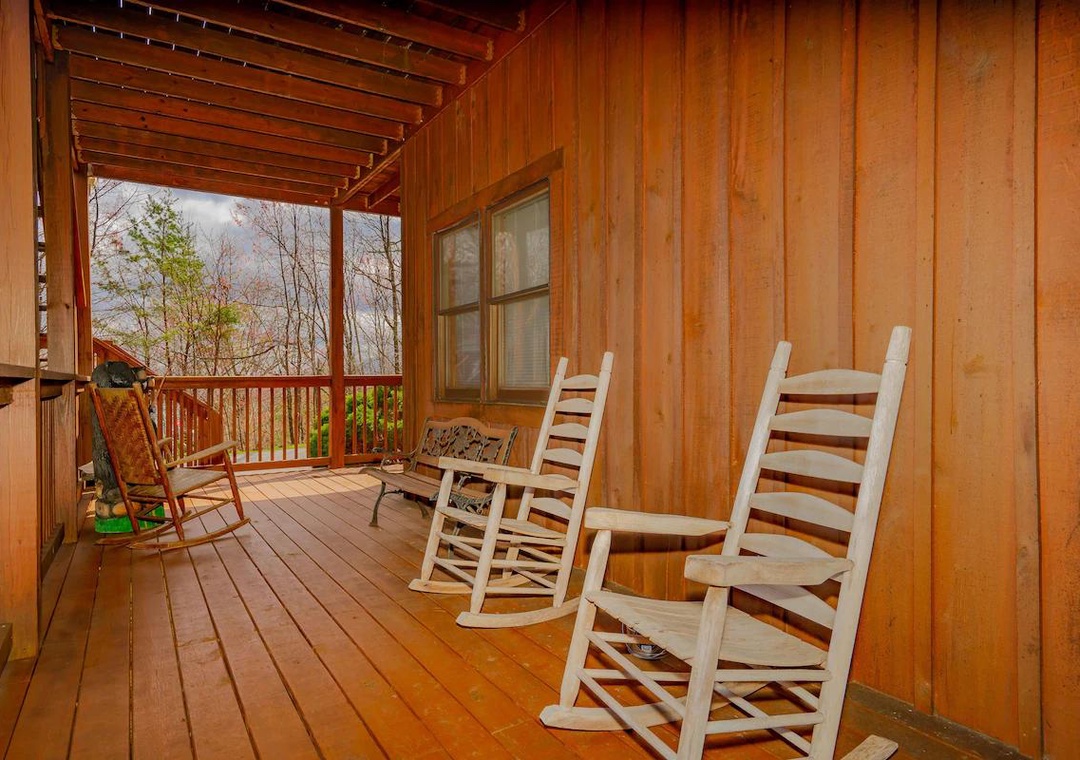 Unwind on your private covered porch with classic rocking chairs, perfect for morning coffee or evening relaxation surrounded by peaceful forest views.