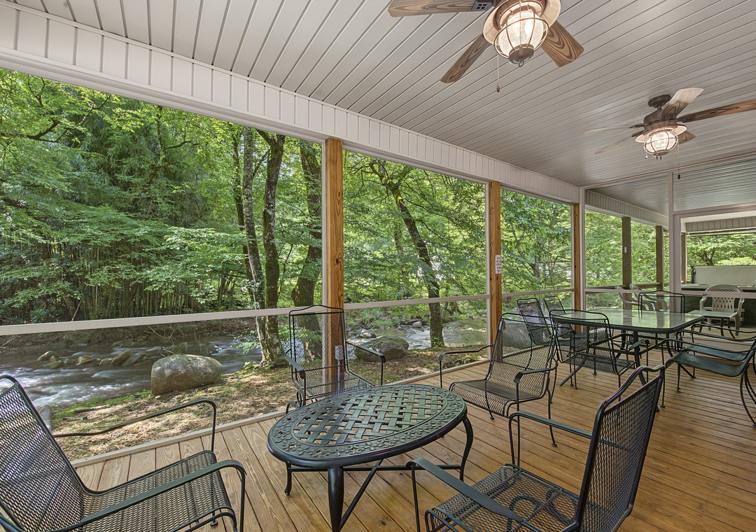 A covered porch with river views offers ample seating for relaxation. Ceiling fans ensure comfort as you unwind beside the flowing water and lush greenery.