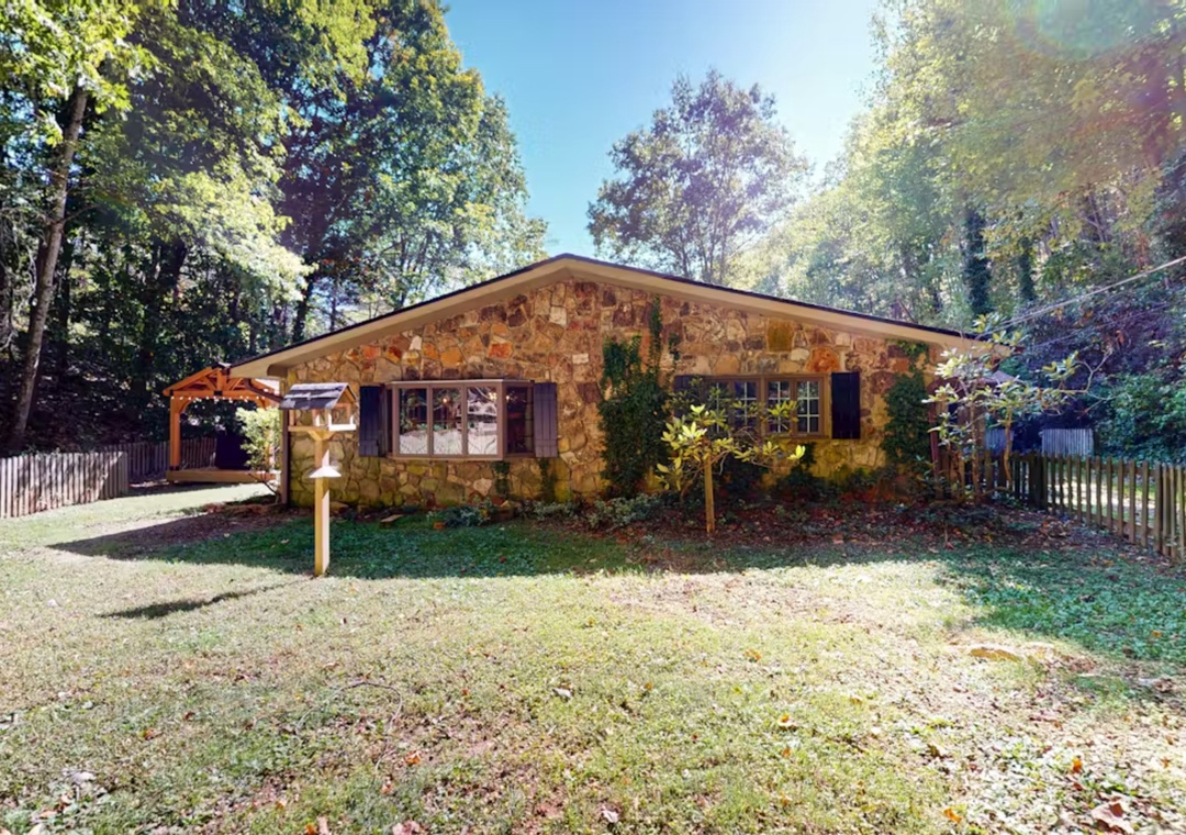 A charming stone cottage nestled among towering trees, featuring rustic architecture with natural materials and a peaceful wooded setting.