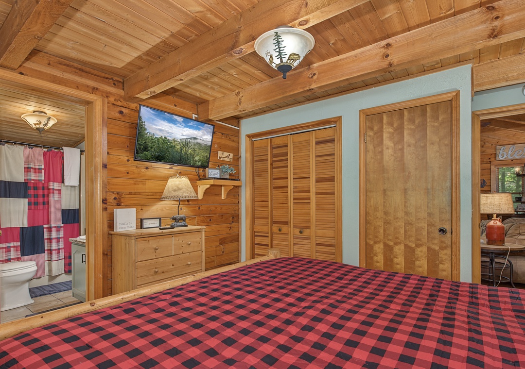Cozy wood-lined bedroom with rustic charm, plaid bedding, and an ensuite bathroom. Natural textures surround you while the warm tones create a mountain cabin feel.