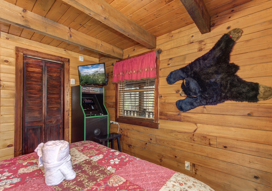 Your cozy cabin bedroom blends rustic charm with fun, featuring warm log walls, arcade gaming, and unique mountain lodge decor.