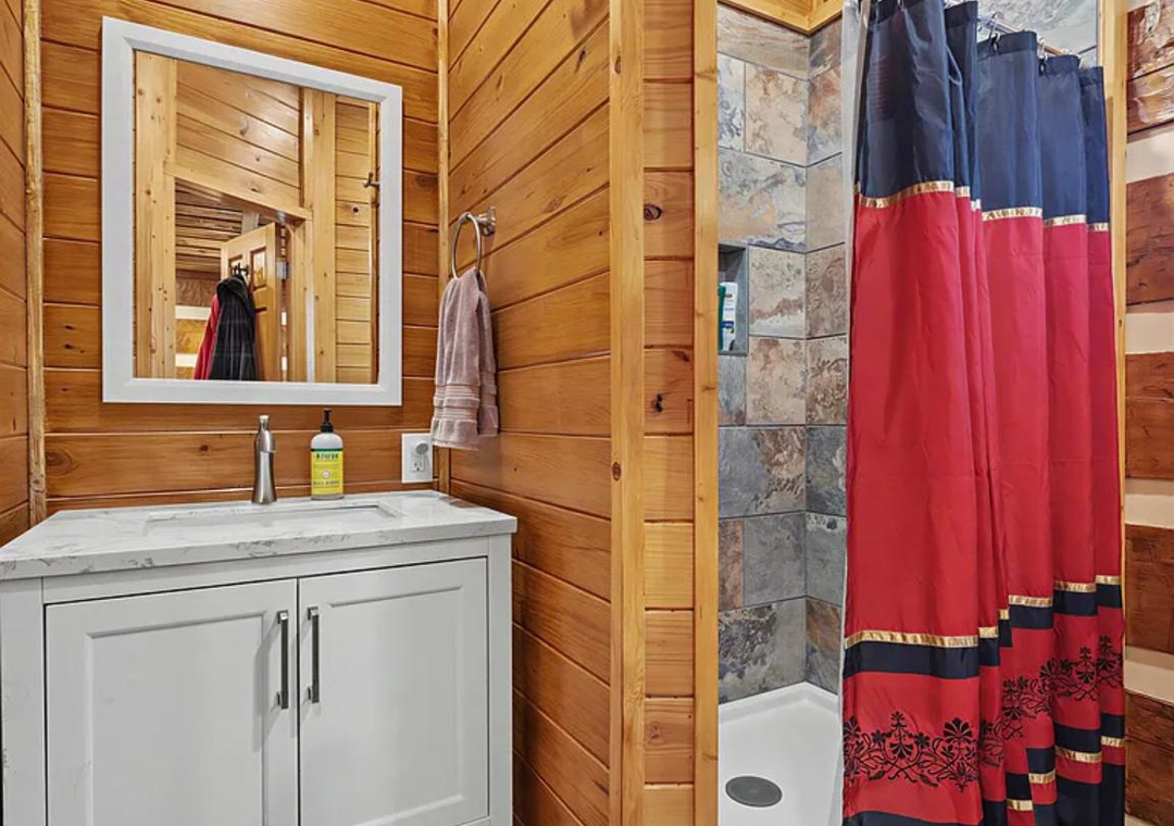 Freshen up in this charming rustic bathroom with warm wood paneling, a marble vanity, and a slate-tiled shower—your private retreat after a day exploring.
