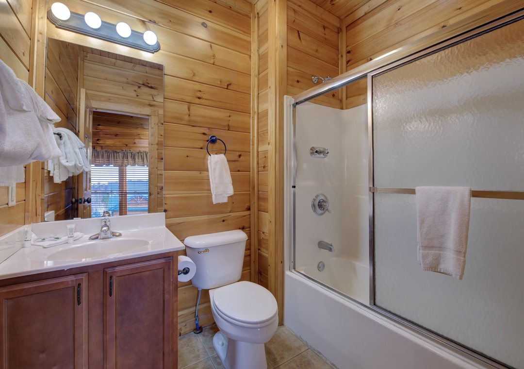 Step into your cozy cabin bathroom with warm wood paneling, a tub-shower combo, and fluffy towels waiting for you after a day of adventure.