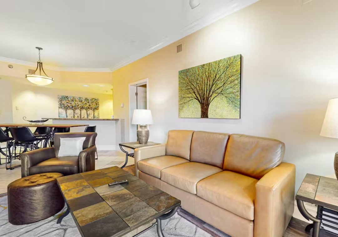 Unwind in your spacious living room featuring plush leather seating, modern artwork, and an open layout that flows into the dining area.