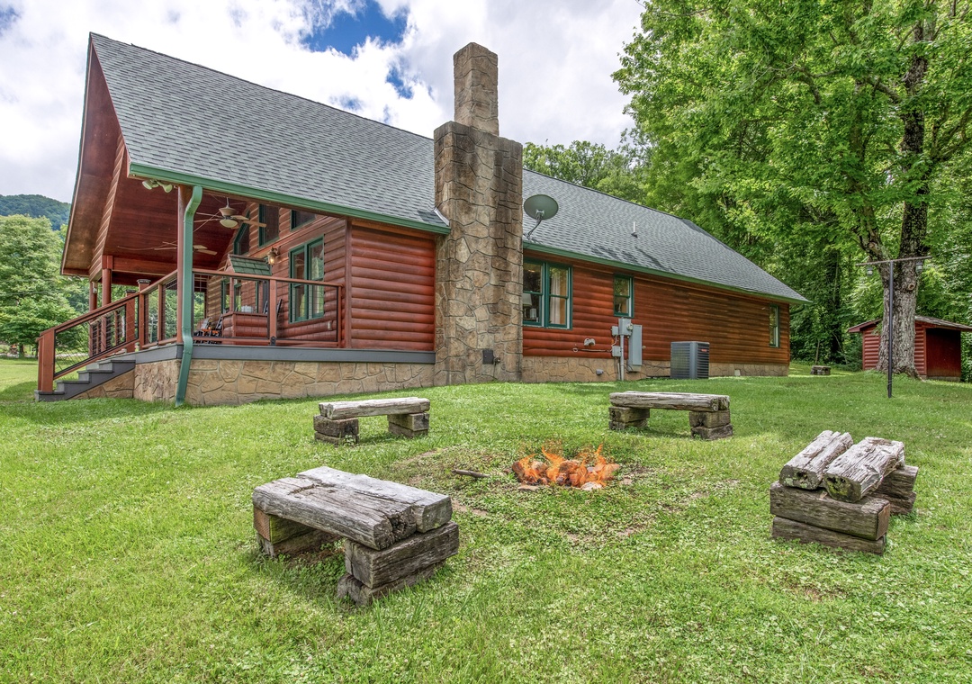 Charming log cabin retreat surrounded by lush greenery and rolling hills, featuring rustic benches around a stone fire pit perfect for evening gatherings under the stars.