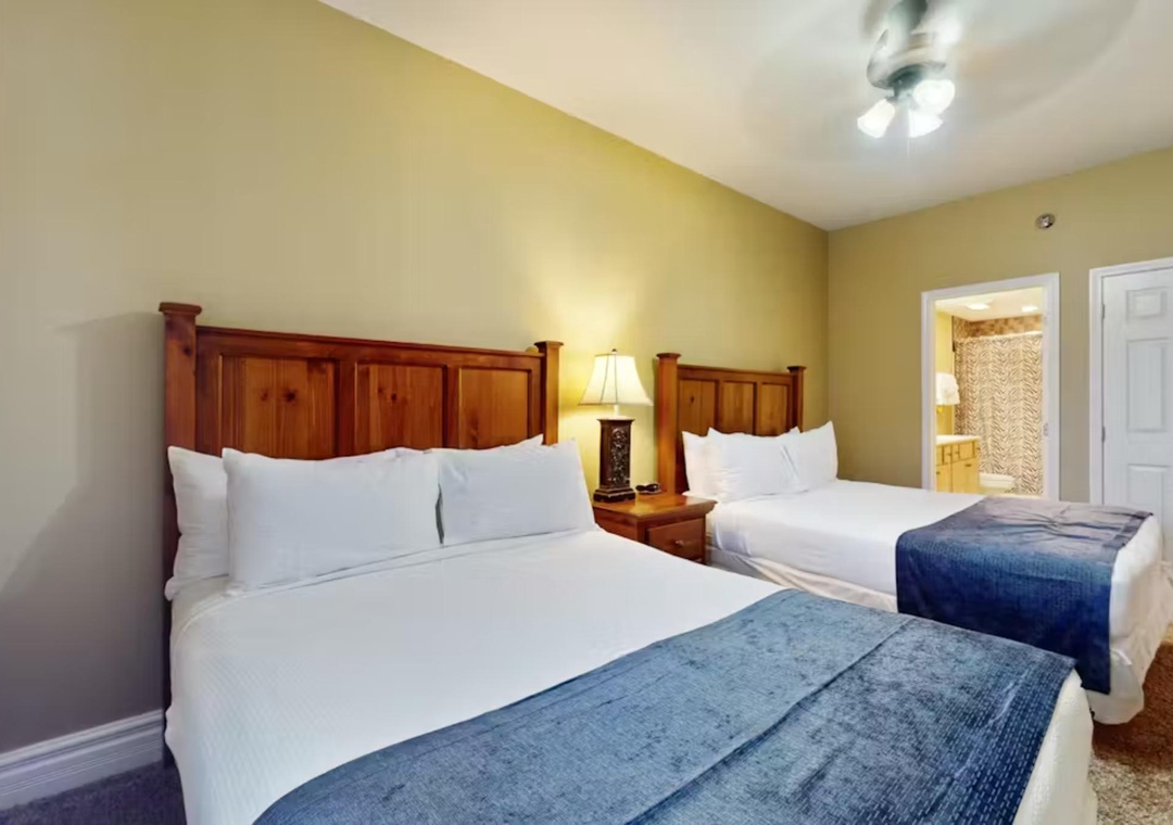 Rest comfortably in your spacious bedroom with two queen beds, warm wood furnishings, and soft linens for a peaceful night's sleep.