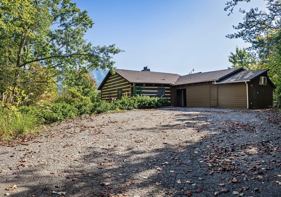 A welcoming log cabin-style retreat set among towering evergreens and lush greenery, offering a peaceful mountain escape with convenient gravel parking and plenty of space to unwind.