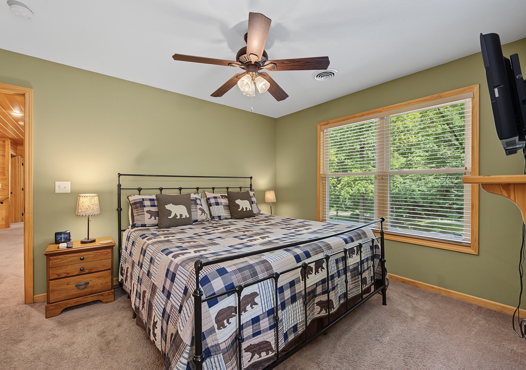 Sink into plush bedding under a gentle ceiling fan as soft natural light filters through the window, framing your peaceful retreat with leafy views and cozy woodland charm.
