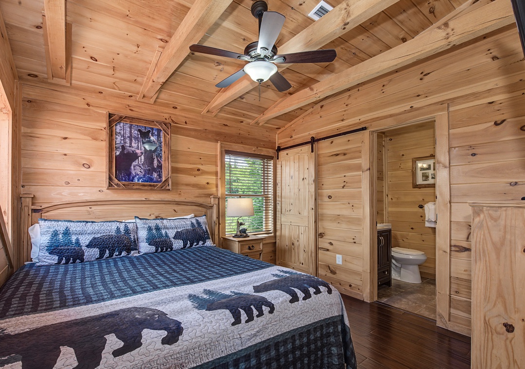 Step into a beautifully crafted cabin bedroom where exposed beam ceilings and warm pine walls embrace you. Your rustic retreat features a plush bed with woodland charm bedding, and a private ensuite just beyond the barn door.