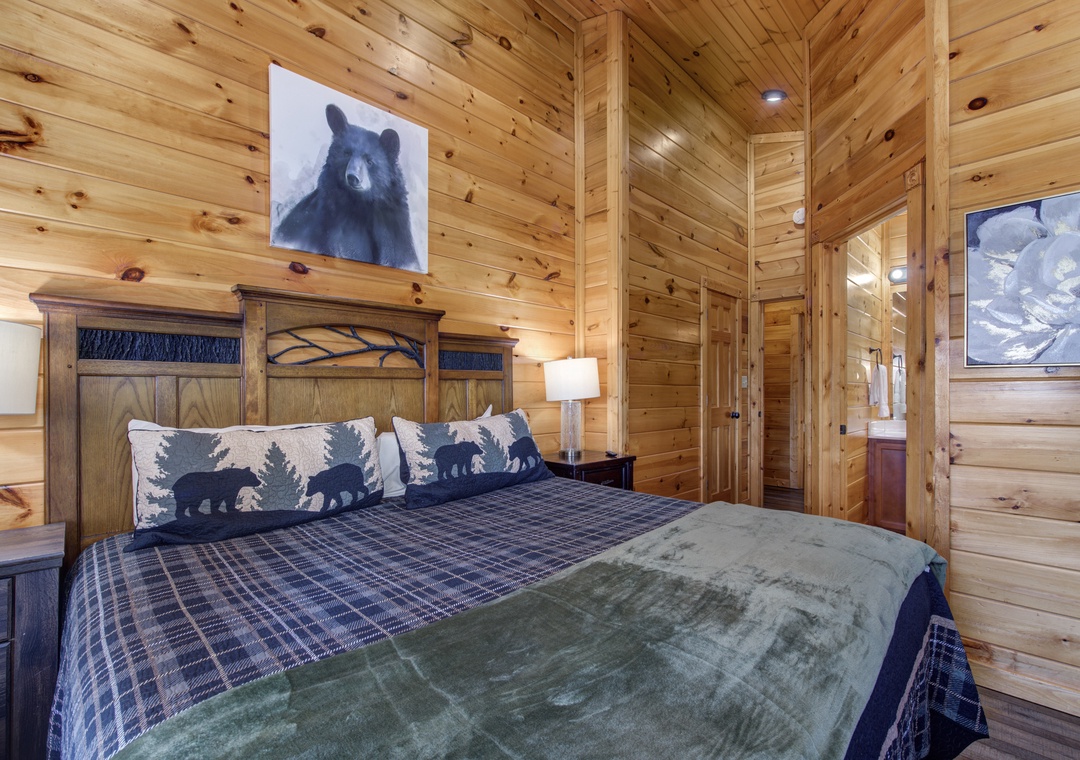 Cozy woodland bedroom with rustic wood-paneled walls and vaulted ceilings. Your charming retreat features a plush bed dressed in plaid linens and bear-themed pillows for mountain cabin charm.