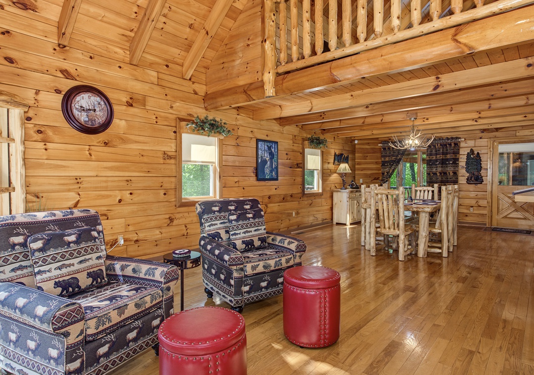 Step into your open-concept lodge-style retreat, where soaring wood-beamed ceilings and warm pine walls create a cozy cabin ambiance. Relax in the inviting living area or gather around the rustic dining table.