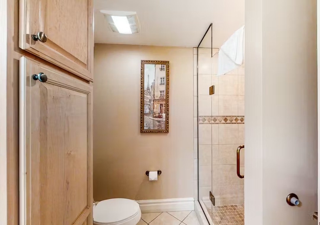 Step into your elegant private bathroom with warm wood cabinetry and a spacious glass-enclosed shower featuring beautiful tile work.