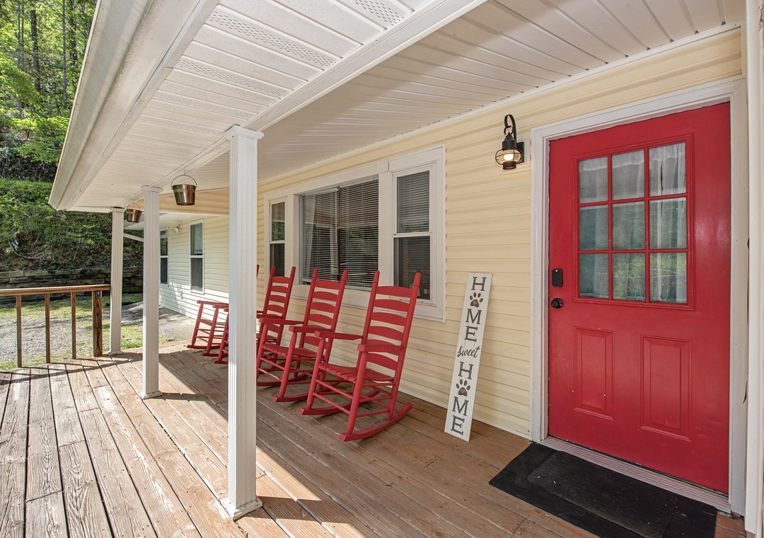 Charming covered porch welcomes you with classic red rocking chairs and a bright red door—perfect for morning coffee and peaceful moments.