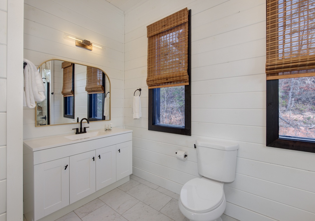 Refresh in your spa-inspired bathroom with crisp white shiplap walls and natural bamboo shades that filter gentle light over peaceful surroundings.