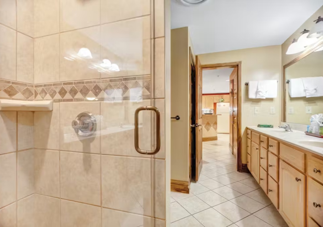 Step into your spacious bathroom with elegant tiled shower, dual vanities, and warm wood finishes for a luxurious daily routine.