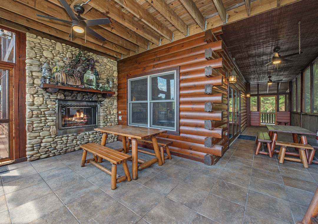 Gather around the stone fireplace in this inviting covered patio, where rustic log benches and soaring wood-beamed ceilings create the perfect setting for your mountain retreat moments.