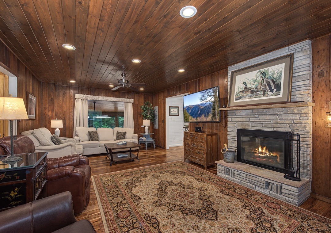 Sink into plush seating in your rustic living room, where rich wood paneling and a crackling stone fireplace create the perfect cozy retreat after exploring the mountains.