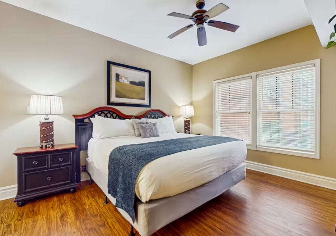 Relax in your elegantly appointed bedroom featuring rich hardwood floors, decorative headboard, and ceiling fan for perfect comfort.