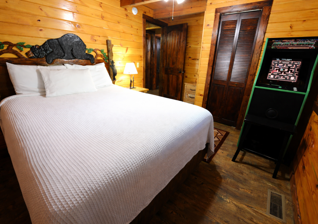 Unwind in your cozy log cabin bedroom featuring rustic charm with a unique carved headboard and vintage arcade game for evening entertainment.