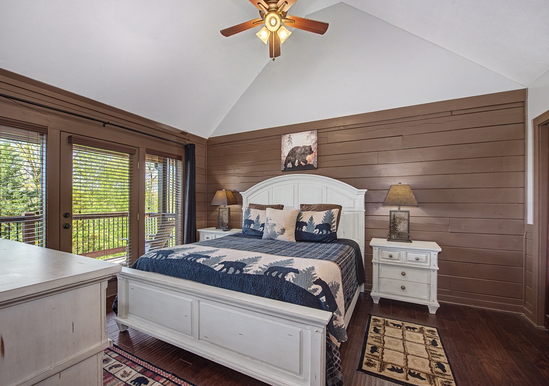 Your cozy mountain bedroom features rustic wood walls, a comfortable queen bed, and peaceful forest views through large windows.