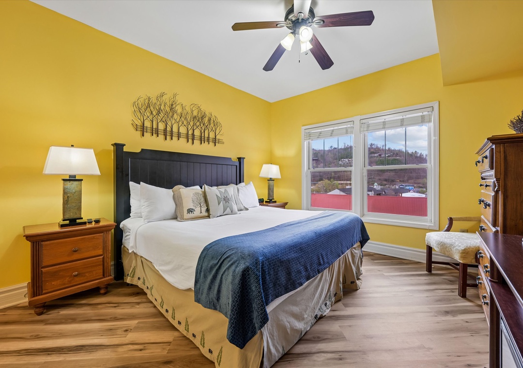 Unwind in your cheerful yellow bedroom featuring a cozy king bed, warm wood furnishings, and peaceful views from your private window.