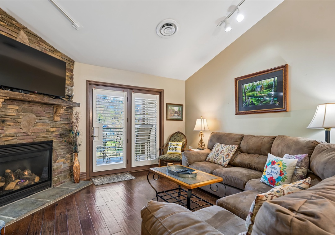 Unwind in your cozy living room featuring a stone fireplace, plush sectional sofa, and private balcony access with peaceful views.
