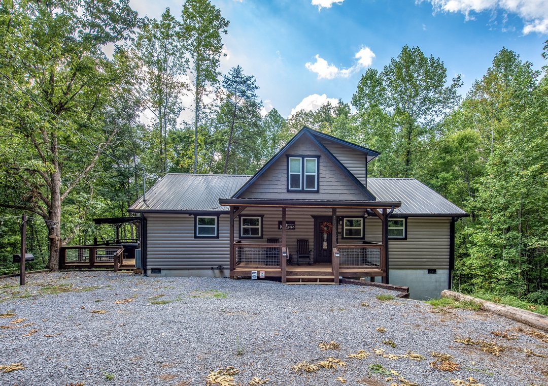 The property sits nestled among towering trees in a peaceful wooded setting, offering a private mountain retreat with ample parking and wraparound outdoor spaces.