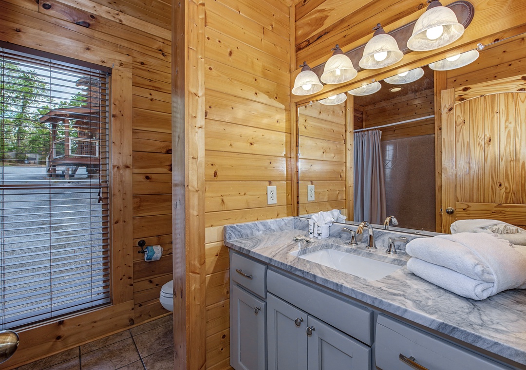 Unwind in your rustic-chic bathroom featuring warm wood walls, elegant marble vanity, and fluffy towels awaiting your arrival.