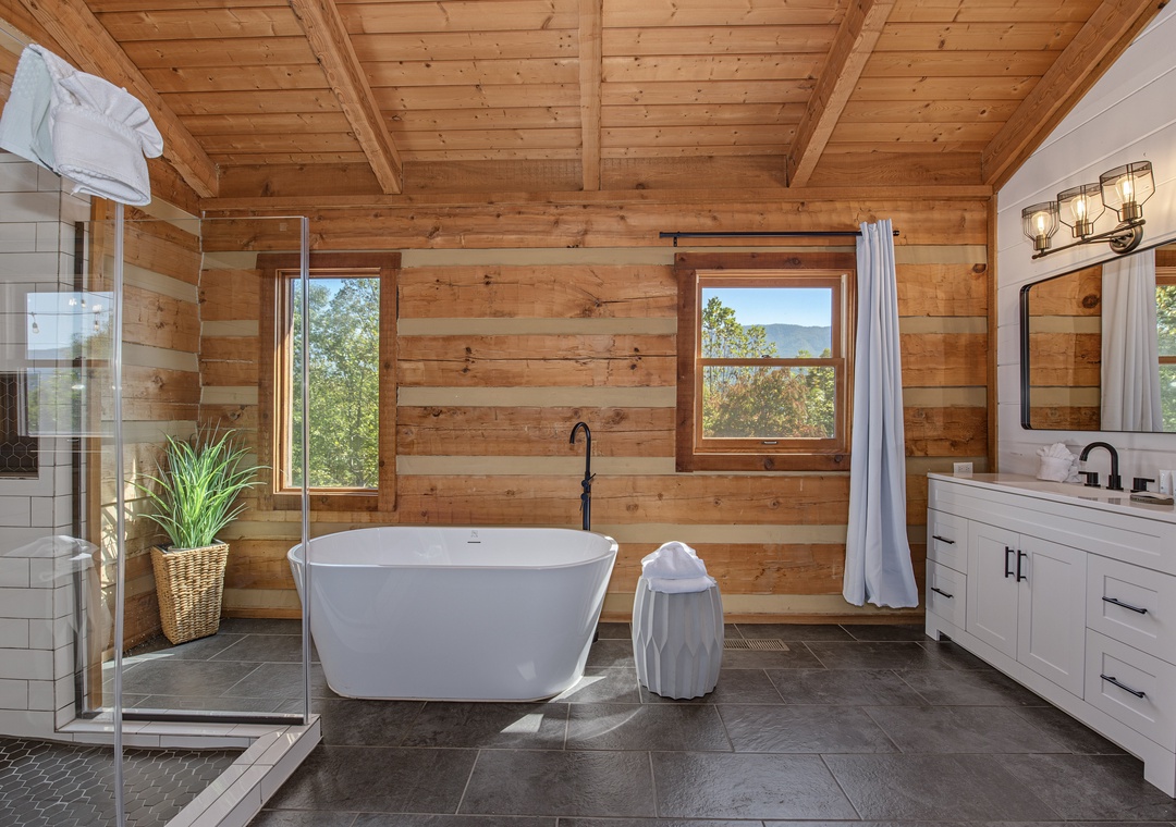 Unwind in this serene spa-like bathroom with warm wood ceilings and a luxurious freestanding tub perfectly positioned to capture views of lush greenery and distant mountains through large picture windows.