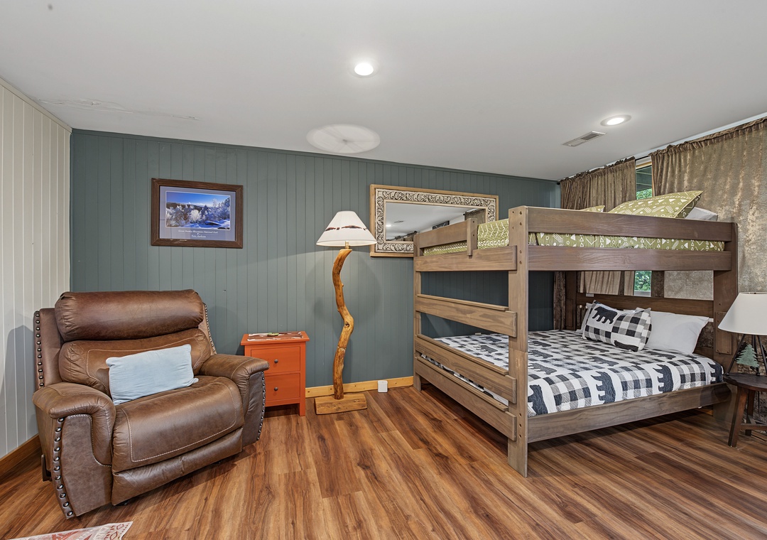 Cozy bedroom with rustic bunk beds and comfortable leather recliner for relaxing. Warm wood floors and mountain-inspired decor create a welcoming retreat for your family.