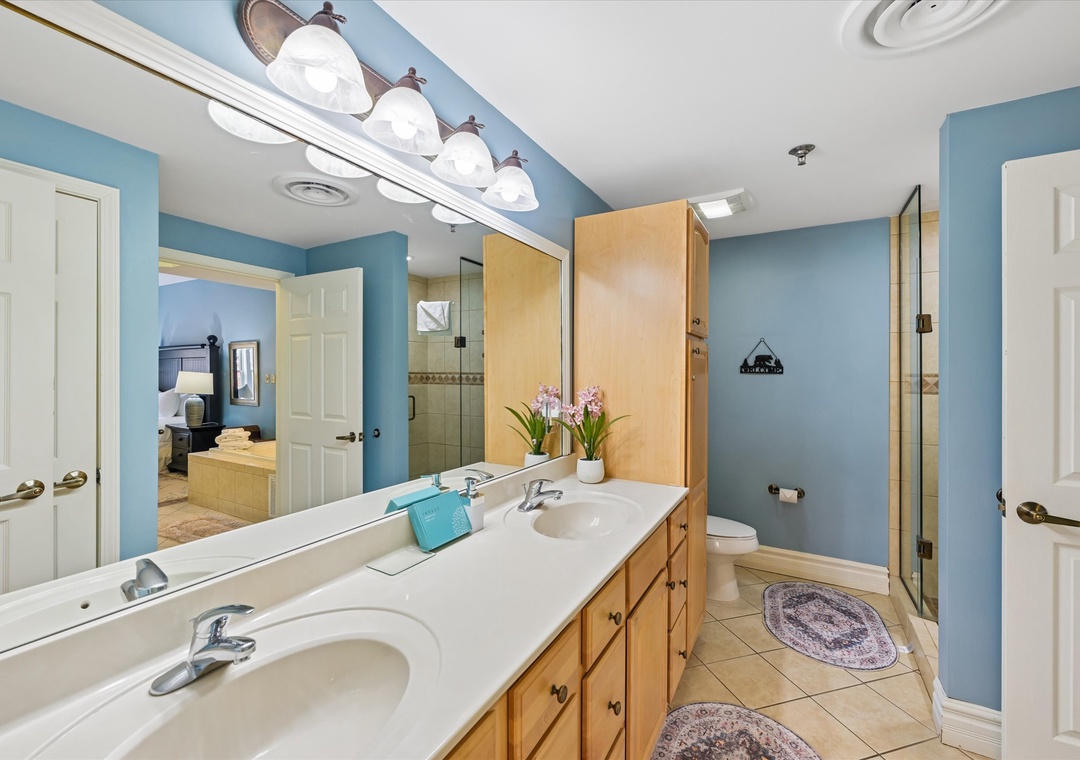 Refresh in your spacious bathroom with dual sinks, warm wood vanity, and calming blue walls that create a spa-like retreat.
