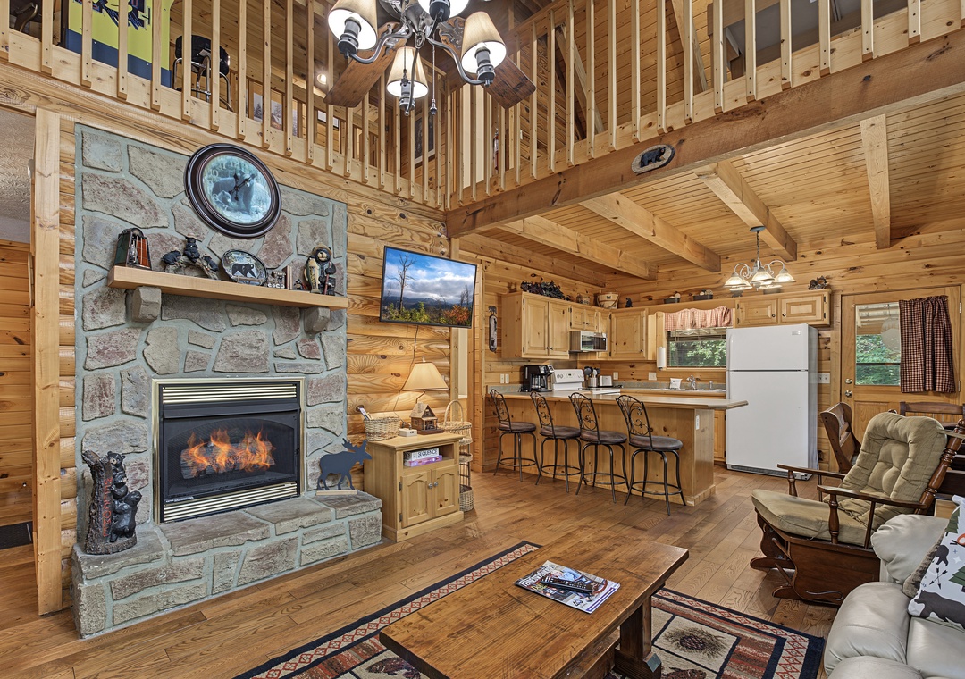 Unwind in your spacious cabin with soaring ceilings and a cozy stone fireplace glowing at the heart of the open living space, seamlessly blending rustic charm with modern comfort.