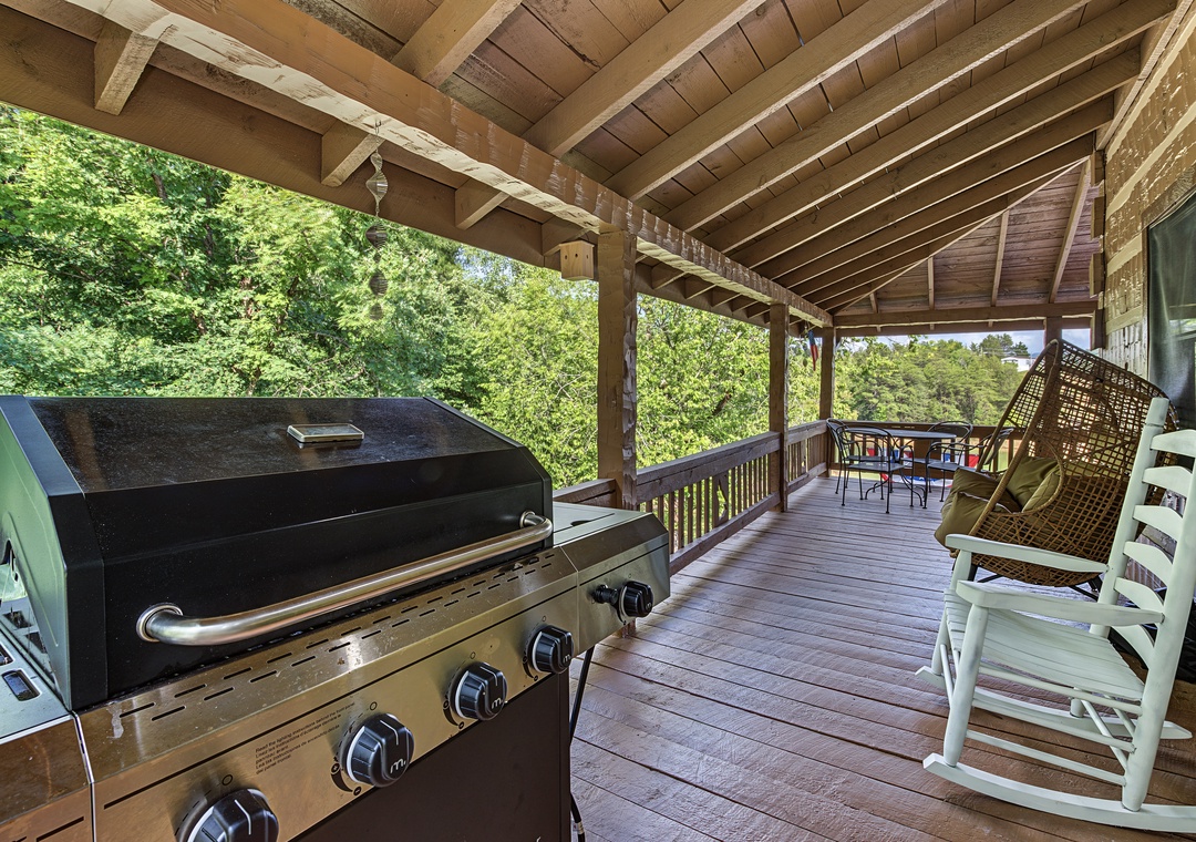Relax in your private covered deck with a gas grill ready for cookouts, rocking chairs for unwinding, and a dining table perfect for meals surrounded by lush forest views.