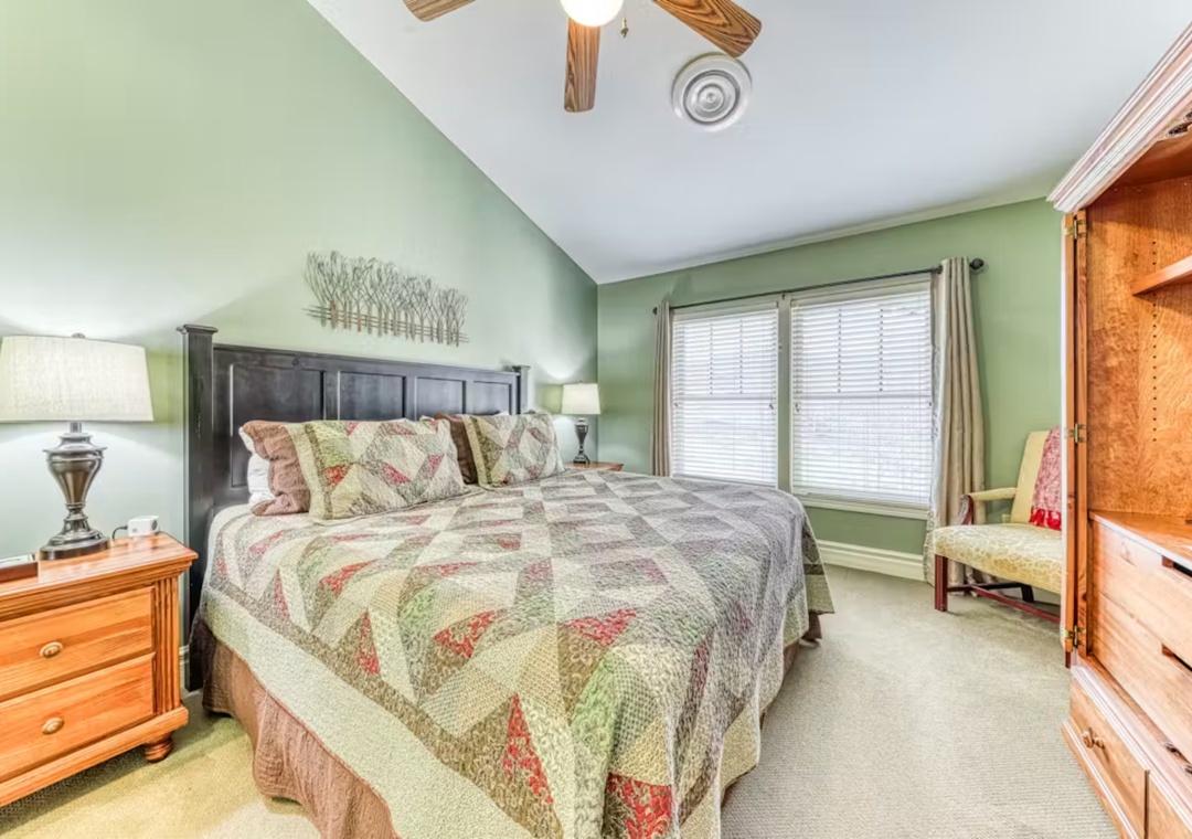 Drift off in your cozy bedroom featuring soft green walls, elegant quilted bedding, and warm wood furnishings that create a peaceful retreat.