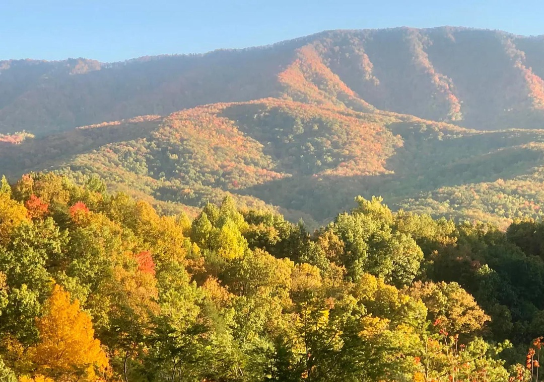 A stunning mountain landscape painted in vibrant autumn hues, with rolling peaks and colorful foliage framing the surrounding area near the property.