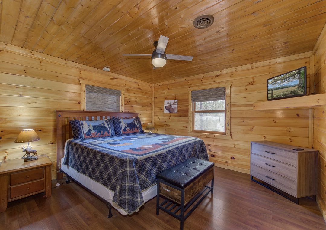 Rest in your cozy log cabin bedroom with warm wood walls, rustic bear-themed bedding, and a gentle ceiling fan for perfect comfort.
