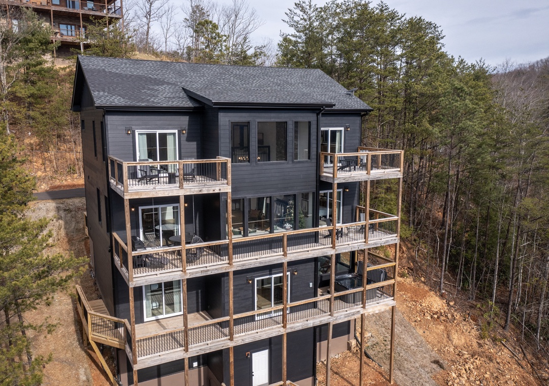 Modern mountain retreat with expansive decks on every level, nestled among towering trees in a peaceful wooded setting.