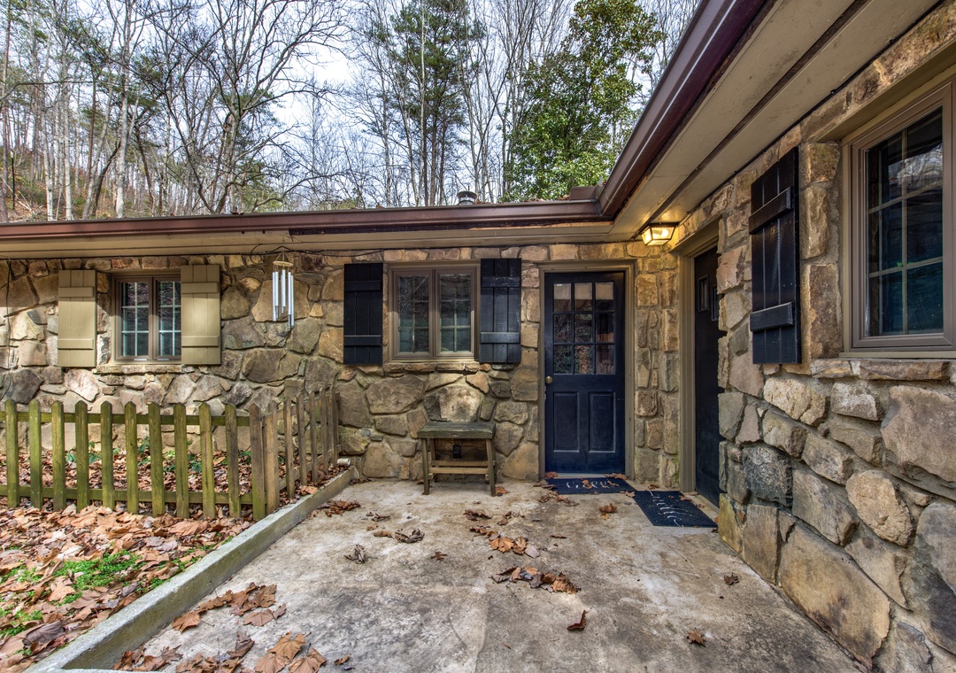 Charming stone cottage facade with rustic architecture nestled among mature trees in a peaceful wooded setting.