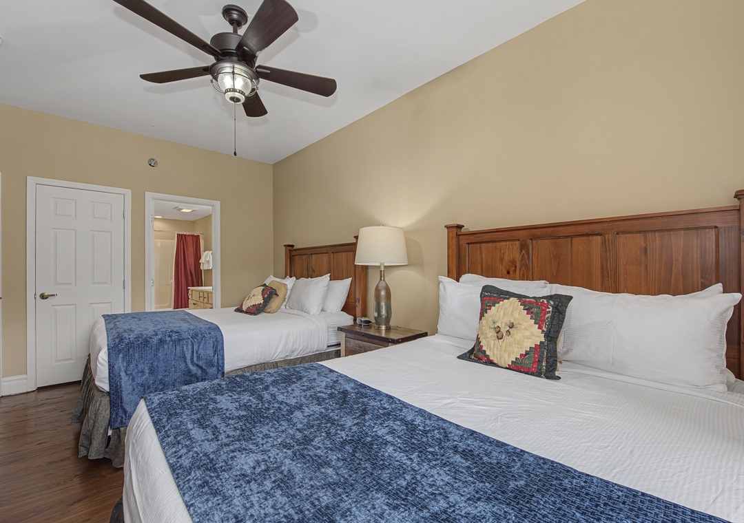 Unwind in your spacious room featuring two comfortable beds with crisp linens and rustic wood headboards beneath a gentle ceiling fan.