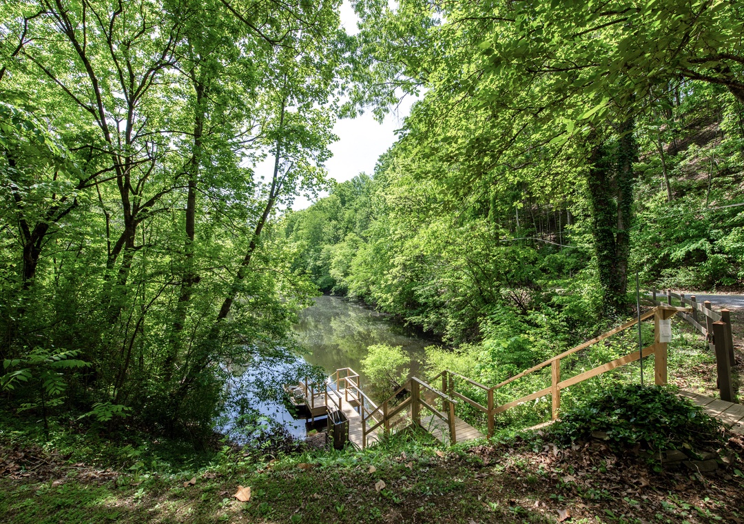 Lush riverside setting surrounded by towering trees and serene natural beauty, with a private dock leading to tranquil waters perfect for peaceful mornings or quiet afternoons.