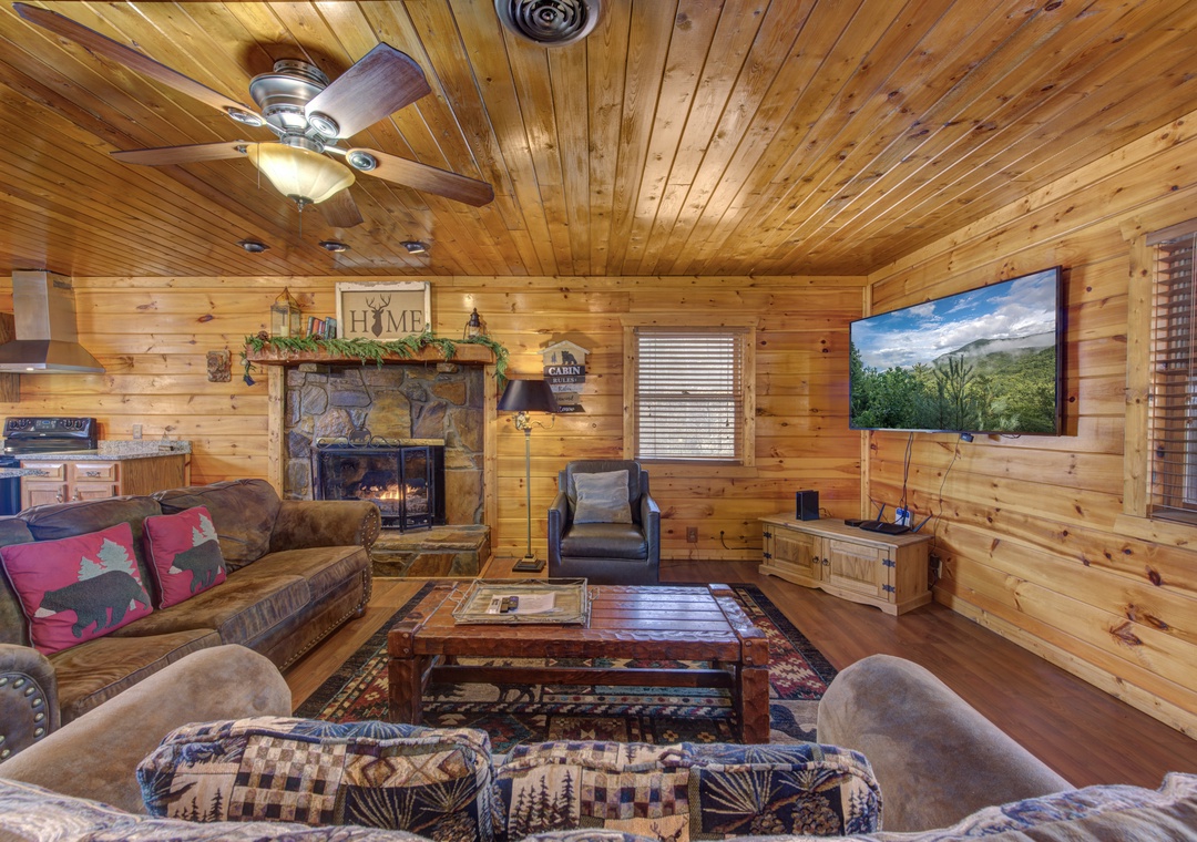 Cozy up in this rustic living room where warm wood surrounds you, a stone fireplace awaits, and mountain views fill the large TV screen.
