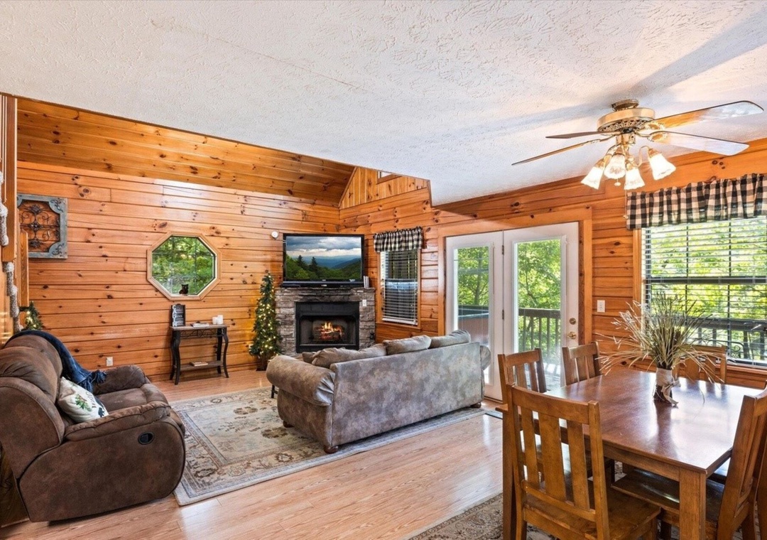 Relax in your cozy cabin living space with rustic wood walls, plush seating around the fireplace, and mountain views through large windows.
