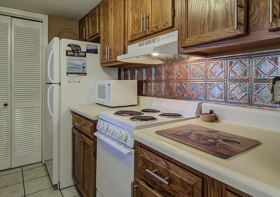 Your fully equipped kitchen features warm wood cabinets and decorative tile backsplash, ready for preparing memorable meals during your stay.