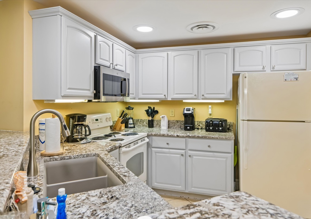 Cook your favorite meals in this fully equipped kitchen with granite counters, white cabinets, and all essential appliances for your stay.